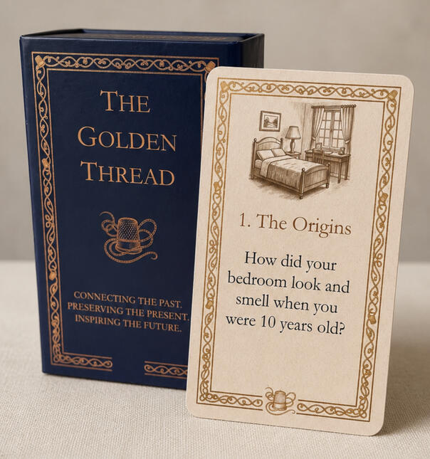 A product hero shot of the Golden Thread showing the deep blue box with golden etching, together with a sample cream coloured card with vintage sepia etching.