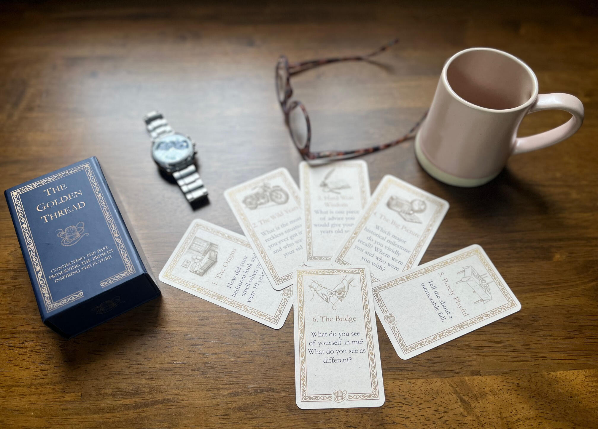 The Golden Thread intergenerational card game box, and a few cards. Deep blue and gold design with sepia vintage etchings
