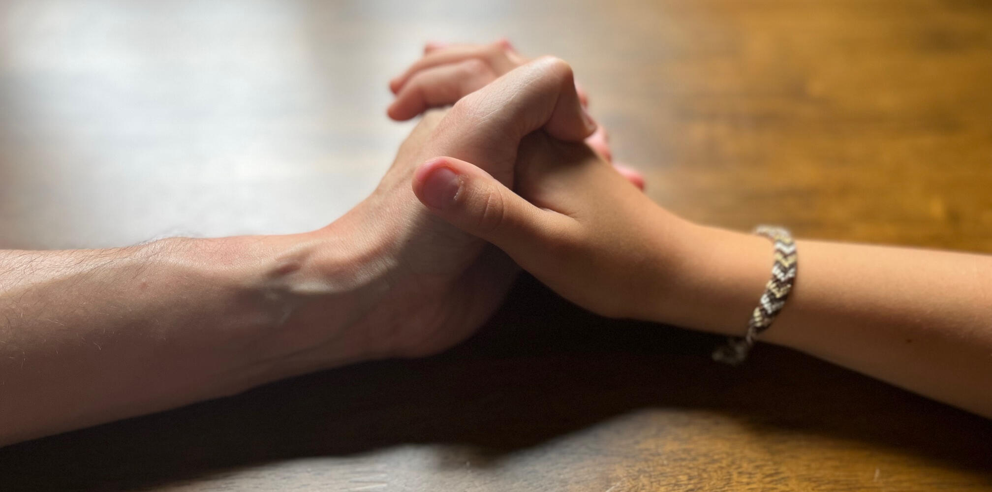 Close shot of an older and a younger hand holding each other to represent the link created between generations when sharing family stories while playing The Golden Thread card game together